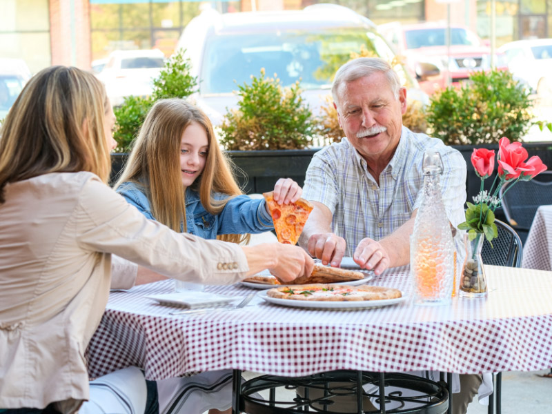 family eating pizza at outside table